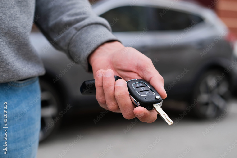 Man in front of the new car and holding keys. Salesman is carrying the car keys delivered to the customer at the showroom with a low interest offer.  Rent, credit, insurance, car purchase. Copy space