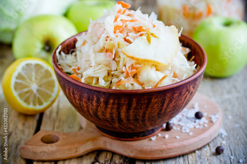 Homemade sauerkraut with green apple and carrot in a clay bowl