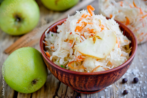 Homemade sauerkraut with green apple and carrot in a clay bowl