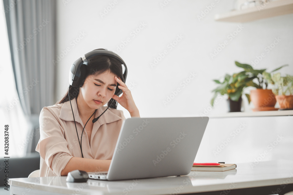 Asian woman with headset exhausted and tired after work via laptop at home having headache problem. Stress form working from home concept Asian woman with headset exhausted and tired after work via laptop at home having headache problem. Stress form working from home concept