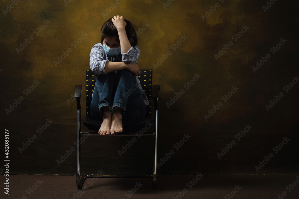 Woman wearing face mask depression scratching her head while sitting on the chair.Depression associated with COVID-19