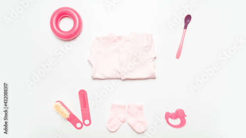 Clothes and accessories for baby. Pink bodusuit and socks, comb, spoon, toys. White background. Flat lay. Mock up