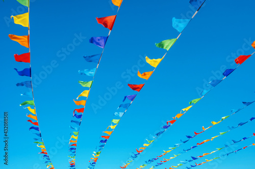 Triangular flags of different colours develop in the wind against the blue clear sky.