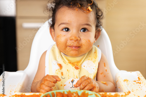 Cute baby in high chair with guilty messy face