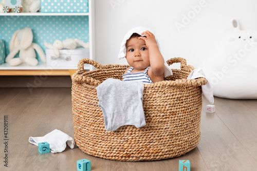 Funny baby sitting in laundry basket with clothes on head photo