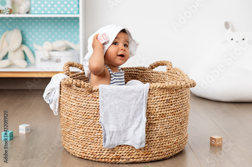 Cute baby sitting in laundry basket with clothes on head photo