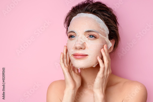 Woman applying cotton facial mask on face. Photo of attractive woman with perfect makeup on pink background. Beauty and Skin care concept