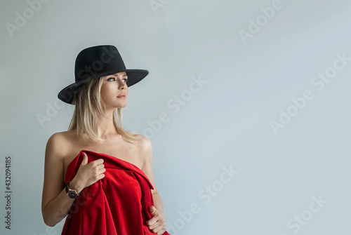 Sexy woman wearing black felt hat covers herself a red coat. On a gray background