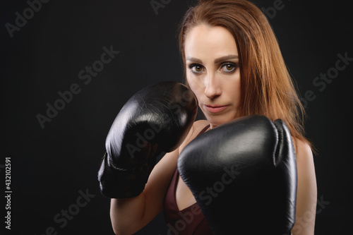 Portrait Caucasian fitness girl in boxing gloves stands in a rack on a black background, portrait of a strong and independent woman fighter © yanik88