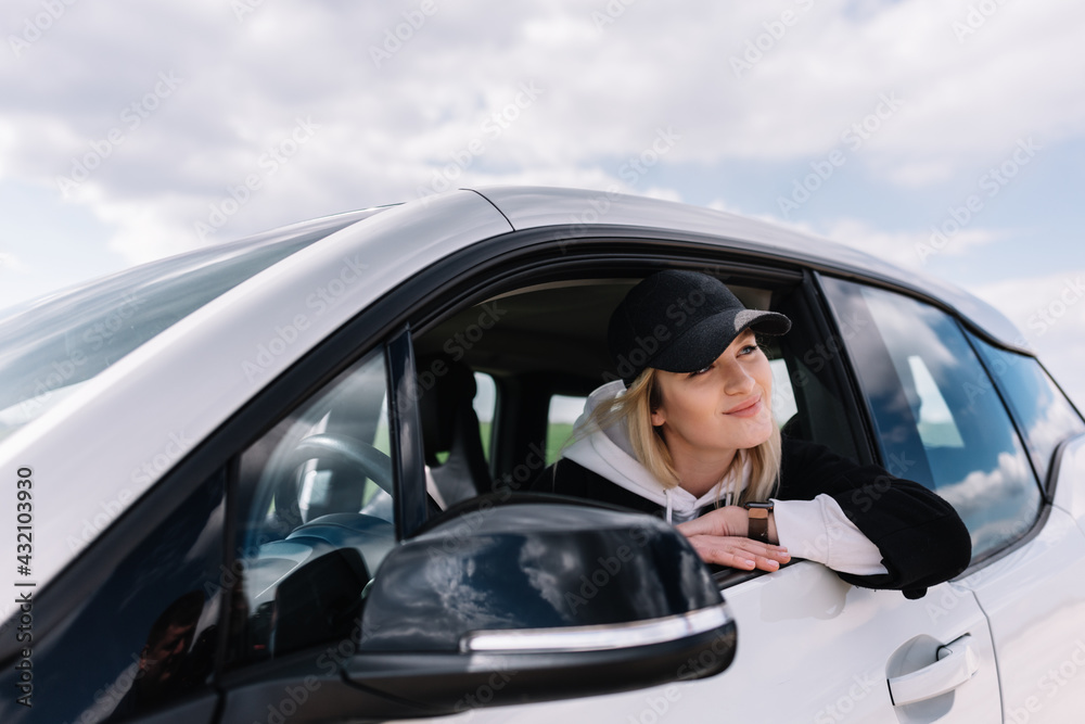 Portrait of a beautiful young woman laughing in a car. A woman takes a break from a road trip. The girl is sitting in black car and looks happily outdoors. Portrait of a beautiful young woman laughing in a car. A woman takes a break from a road trip. The girl is sitting in black car and looks happily outdoors.