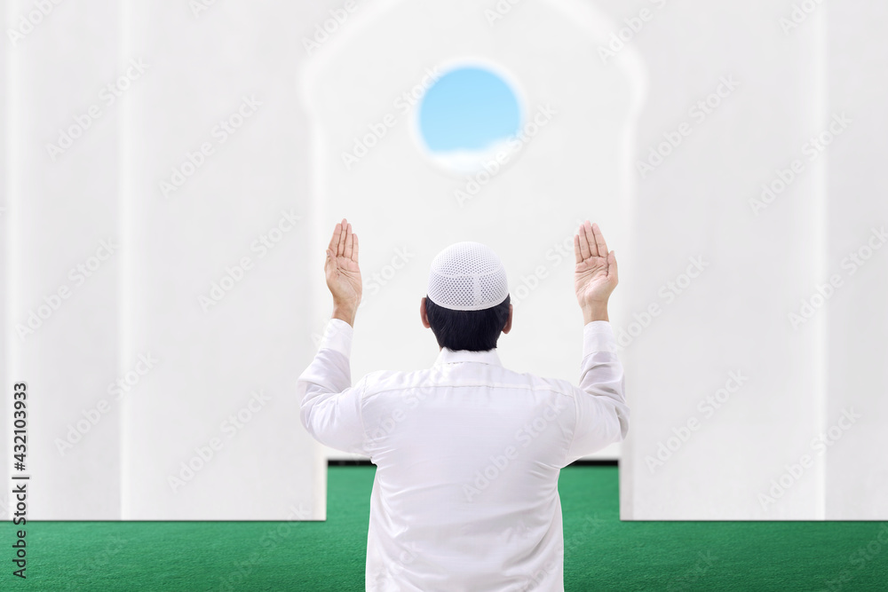 Rear view of Asian Muslim man sitting while raised hands and praying Rear view of Asian Muslim man sitting while raised hands and praying