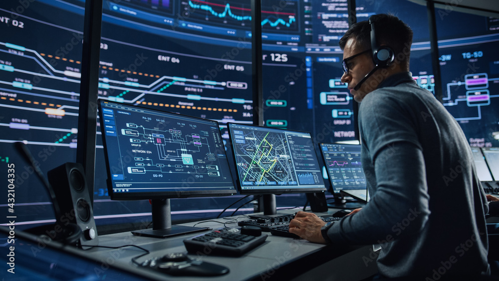 Professional IT Technical Support Specialist and Software Developer Working on Computer in Monitoring Control Room with Digital Screens. Employee Wears Headphones with Mic and Talking on a Call. Professional IT Technical Support Specialist and Software Developer Working on Computer in Monitoring Control Room with Digital Screens. Employee Wears Headphones with Mic and Talking on a Call.