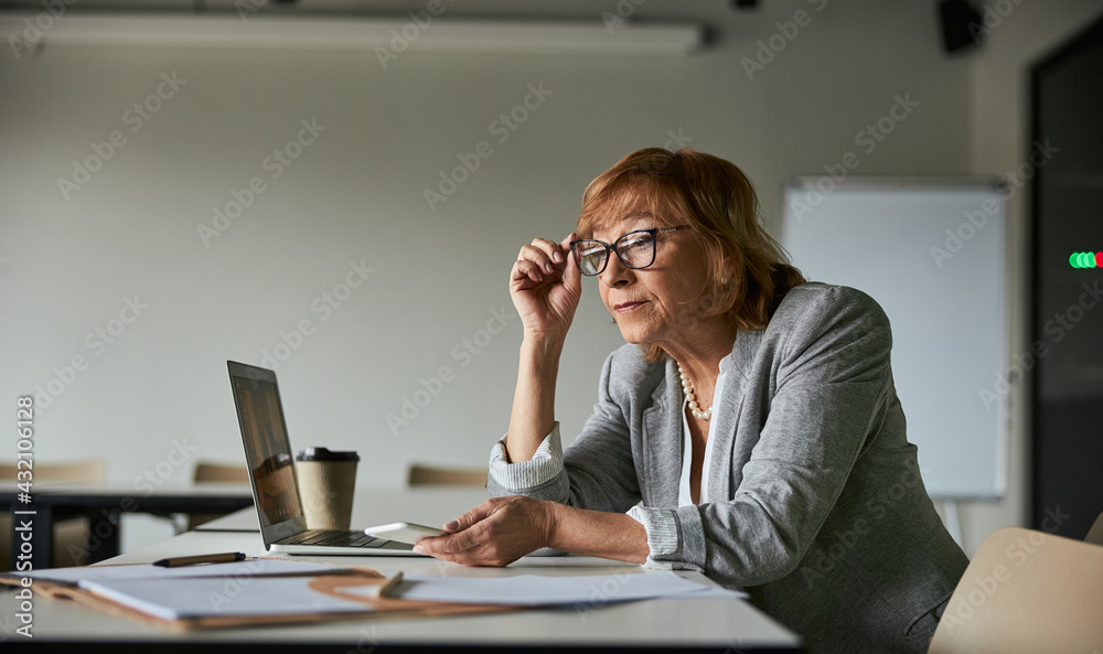 Female adjusting her glasses while reading paper records Female adjusting her glasses while reading paper records