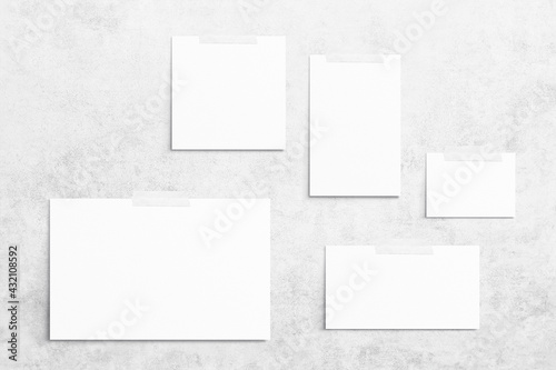 Composition of 5 empty white different sizes watercolor sheets of paper glued with scotch tape on light gray concrete background. Advertising board, mockup on the wall. Flat lay, top view, copy space