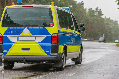 Asphalted road surface in rainy weather. Police car on the Autobahn in the state of Brandenburg. Angled view of the vehicle from behind. Vehicles on the dual lane lane in the background