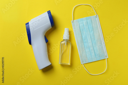 Medical tools and thermometer gun on yellow background