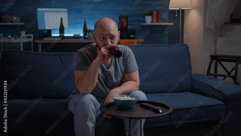 Amused man laughing watching comedy movie on TV eating popcorn and drinking beer. Excited home alone person enjoying the evening at home sitting on comfortable couch dressed in pajamas. Amused man laughing watching comedy movie on TV eating popcorn and drinking beer. Excited home alone person enjoying the evening at home sitting on comfortable couch dressed in pajamas.