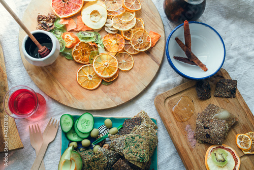 Still life with vegan snacks: dried fruits, crispy crackers, fresh vegetables, fruit candies, honey, juice, tea on a rough fabric. photo