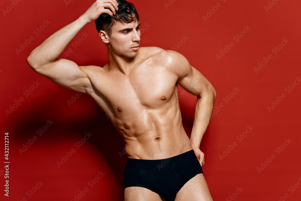 Fototapeta premium naked guy in black shorts holds his hand on his head on a red background pose model torso bodybuilder