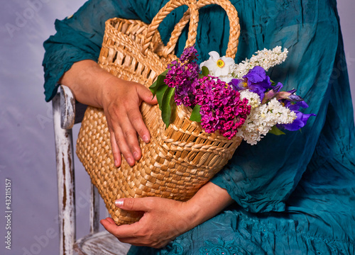 Woman holding hands wicker bag with lilac flowers indoor, Sitting on a vintage chair photo