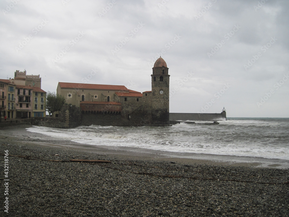 Scenic view of historical castle on the town shore in Collioure, France. Dynamic gray coastline background with storm of the Mediterranean Sea on a cloudy rainy day.