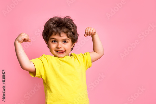 Portrait of little kid boy isolated over pink background showing tongue. Funny little power super hero kid showing muscles. Strength, confidence or defense from bullying. Kindergarten or school kid. photo