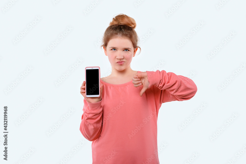 Portrait of a cute young girl holding smartphone and showing thumb down. White background Portrait of a cute young girl holding smartphone and showing thumb down. White background