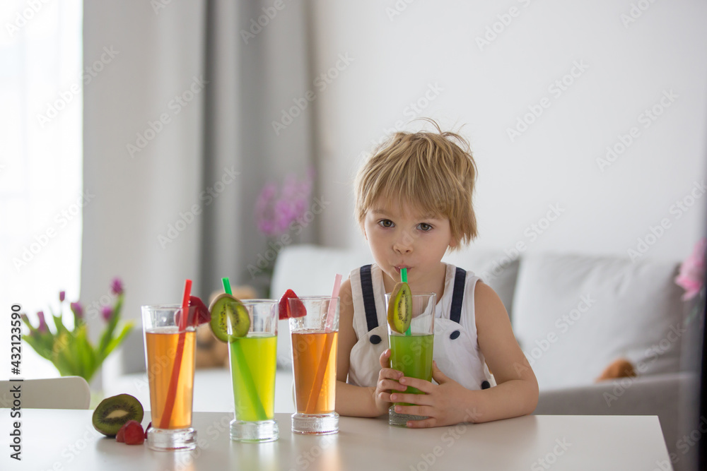 Cute toddler child, blond boy, drinking freshly made fruit juice at home