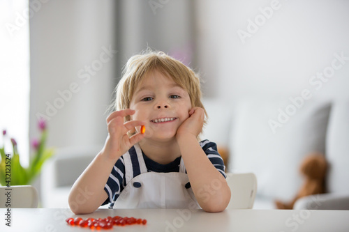 Cute little child, toddler boy, eating alfa omega 3 child supplement vitamin pills at home