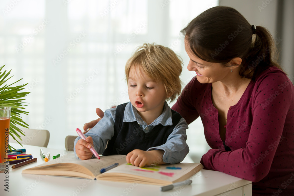 Cute preschool child, blond boy, filling some homework in a work book and coloring, mother helping him Cute preschool child, blond boy, filling some homework in a work book and coloring, mother helping him