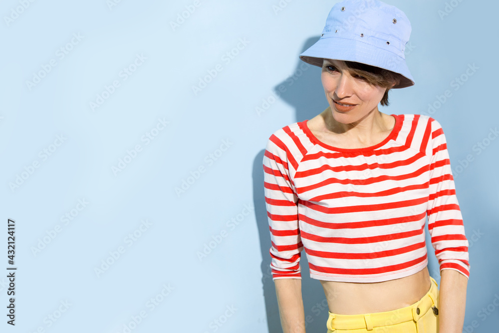 Happy cheerful young woman with short hair, natural makeup over light blue background. Indoor portrait of beautiful brunette young woman wearing blue hat and bright clothing Happy cheerful young woman with short hair, natural makeup over light blue background. Indoor portrait of beautiful brunette young woman wearing blue hat and bright clothing