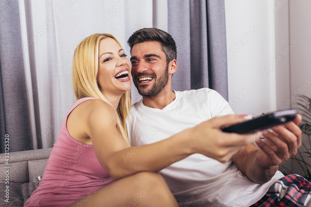 Fototapeta premium Happy couple watching films on tv in bed