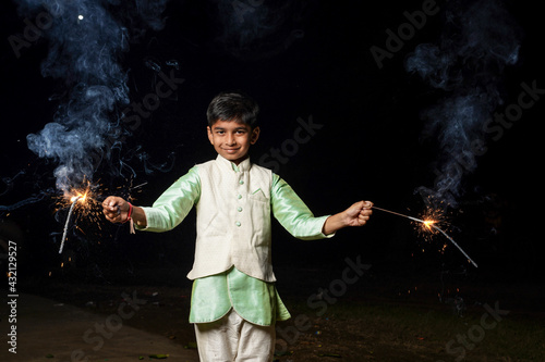 Cute Indian child celebrating Diwali festival with cracker and sparkle
