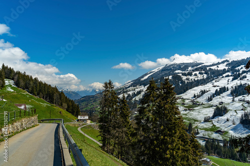 Auf der Strasse von Adelboden nach Frutigen im Berner Oberland. der Tschechen und die Berge dahinter sind noch im Frühling schneebedeckt. an den steilen Hängen stehen Bauernhäuser. photo