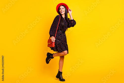 Full length photo of pretty cute lady dressed black clothes arm cap handbag looking empty space isolated yellow color background