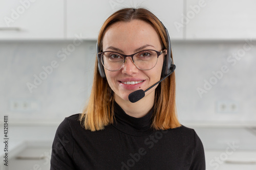 A young happy girl in glasses and a headset smiles and looks directly at the camera. The concept of remote work and learning. High quality photo
