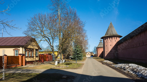 Street of Suzdal, Red Wall and towers of Saint Euthymius monastery, residential russian traditional house across road in sunny day in spring middle april, Golden Ring of Russia photo