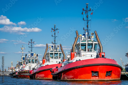 front view of a group of three strong red and white colored tug boats docked in a line in the port of hamburg at neue schlepperbrücke