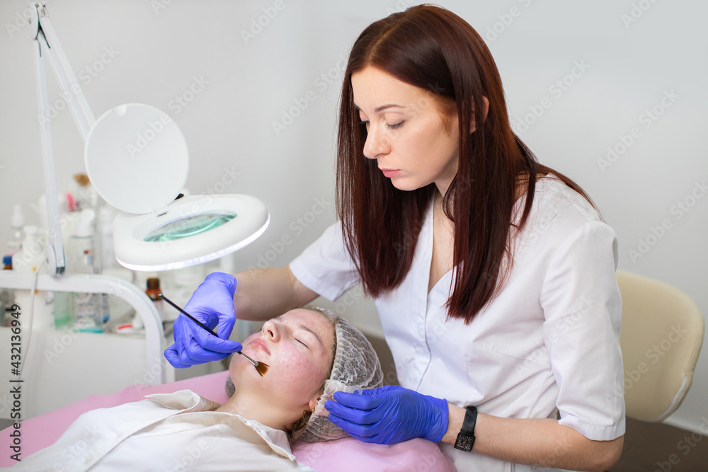 Hydration and acne treatment of the skin. Young female cosmetologist in medical gloves applies gel mask to the face of young teen girl with a brush. Hydration and acne treatment of the skin. Young female cosmetologist in medical gloves applies gel mask to the face of young teen girl with a brush.