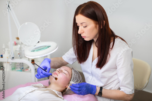 Hydration and acne treatment of the skin. Young female cosmetologist in medical gloves applies gel mask to the face of young teen girl with a brush.
