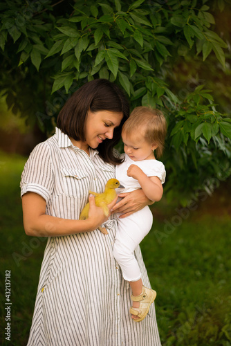 mom holds her daughter in her arms, the weather is warm outside, playing with a duck. mother's day 