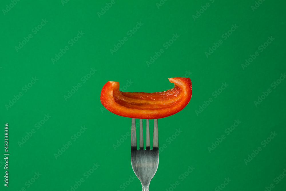 Sweet bell pepper on a fork on a green background in a close-up Sweet bell pepper on a fork on a green background in a close-up