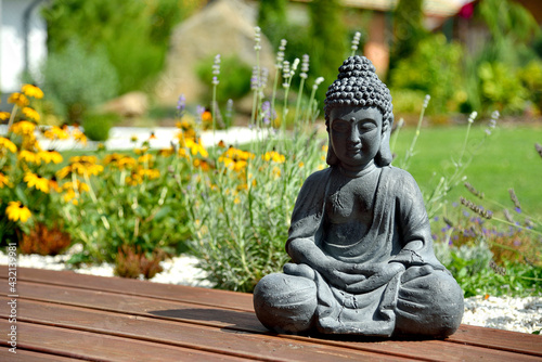 A closeup of a small Buddha statue in a garden with a blurry background