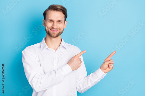 Photo of happy charming young man point index fingers empty space good mood isolated on blue color background