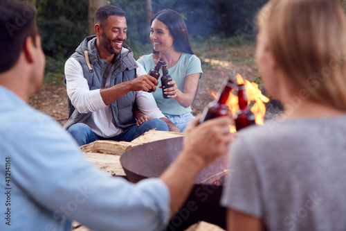Group Of Friends Camping Sitting By Bonfire In Fire Bowl Celebrating And Drinking Beer Together