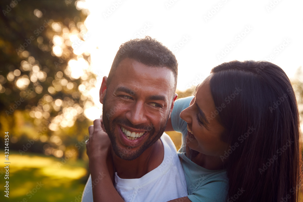 Portrait Of Loving Couple In Countryside With Man Giving Woman Ride On Back Against Flaring Sun Portrait Of Loving Couple In Countryside With Man Giving Woman Ride On Back Against Flaring Sun