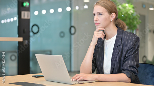 Attractive Young Businesswoman Thinking and Working on Laptop in Office 