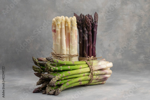 Three bunches of different fresh asparagus isolated on grey. Purple white and green asparagus.