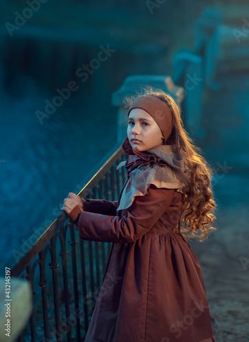 Obraz na płótnie A girl in a brown coat on the bridge by the water in the evening w salonie