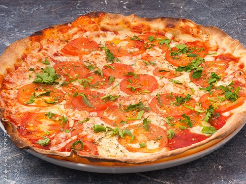 pizza Margarita with tomatoes and mozzarella cheese decorated with greens